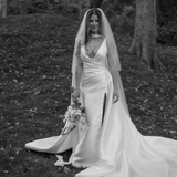 Bride wearing the Heirloom modern A-line wedding dress with veil and leg split, holding a bouquet in an outdoor garden setting.