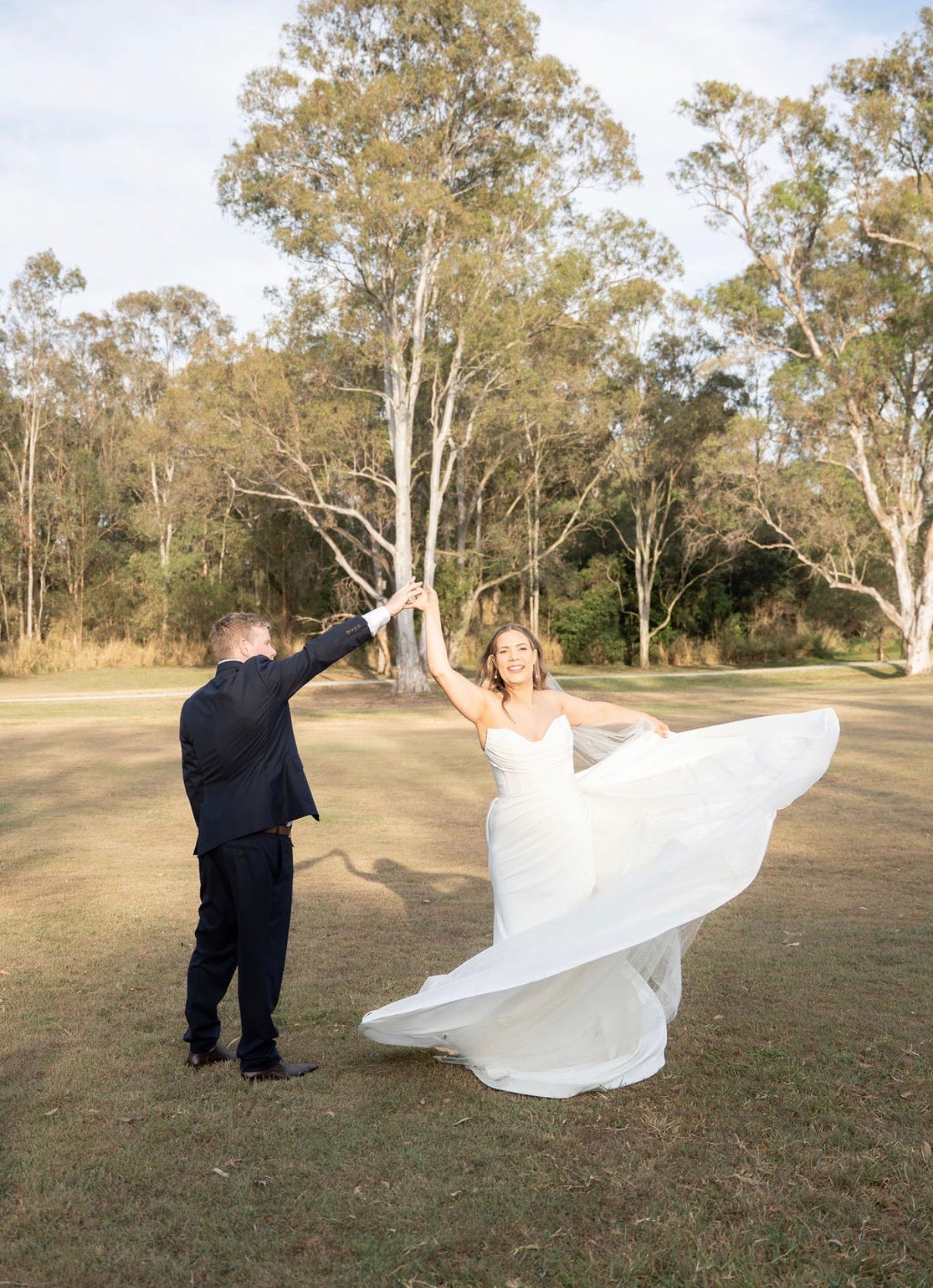 Man lifting a woman in a Fit and Flare Wedding Dress with Overskirt in an outdoor setting with trees.