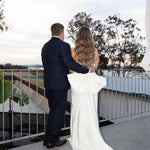 Man and woman in Fit and Flare Wedding Dress with Overskirt and suit standing on a balcony with a scenic view.