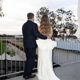 Man and woman in Fit and Flare Wedding Dress with Overskirt and suit standing on a balcony with a scenic view.