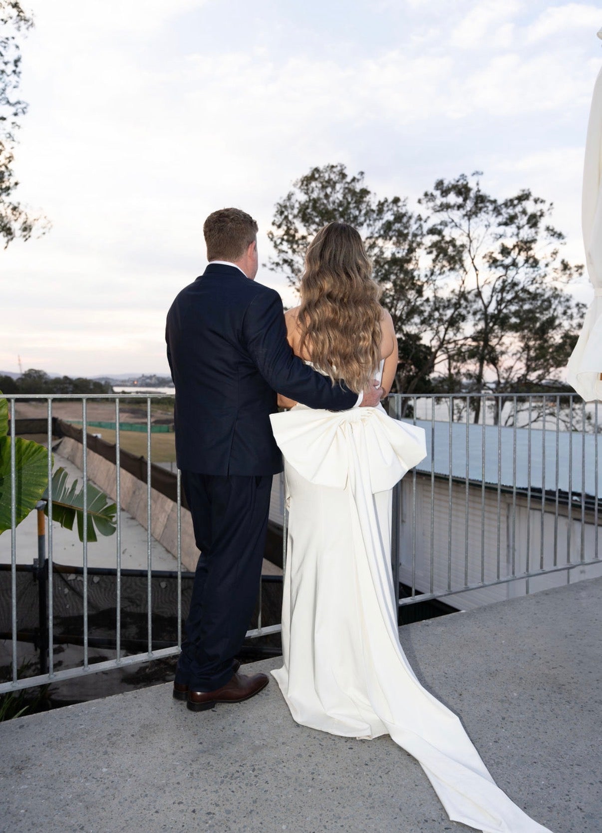 Man and woman in Fit and Flare Wedding Dress with Overskirt and suit standing on a balcony with a scenic view.