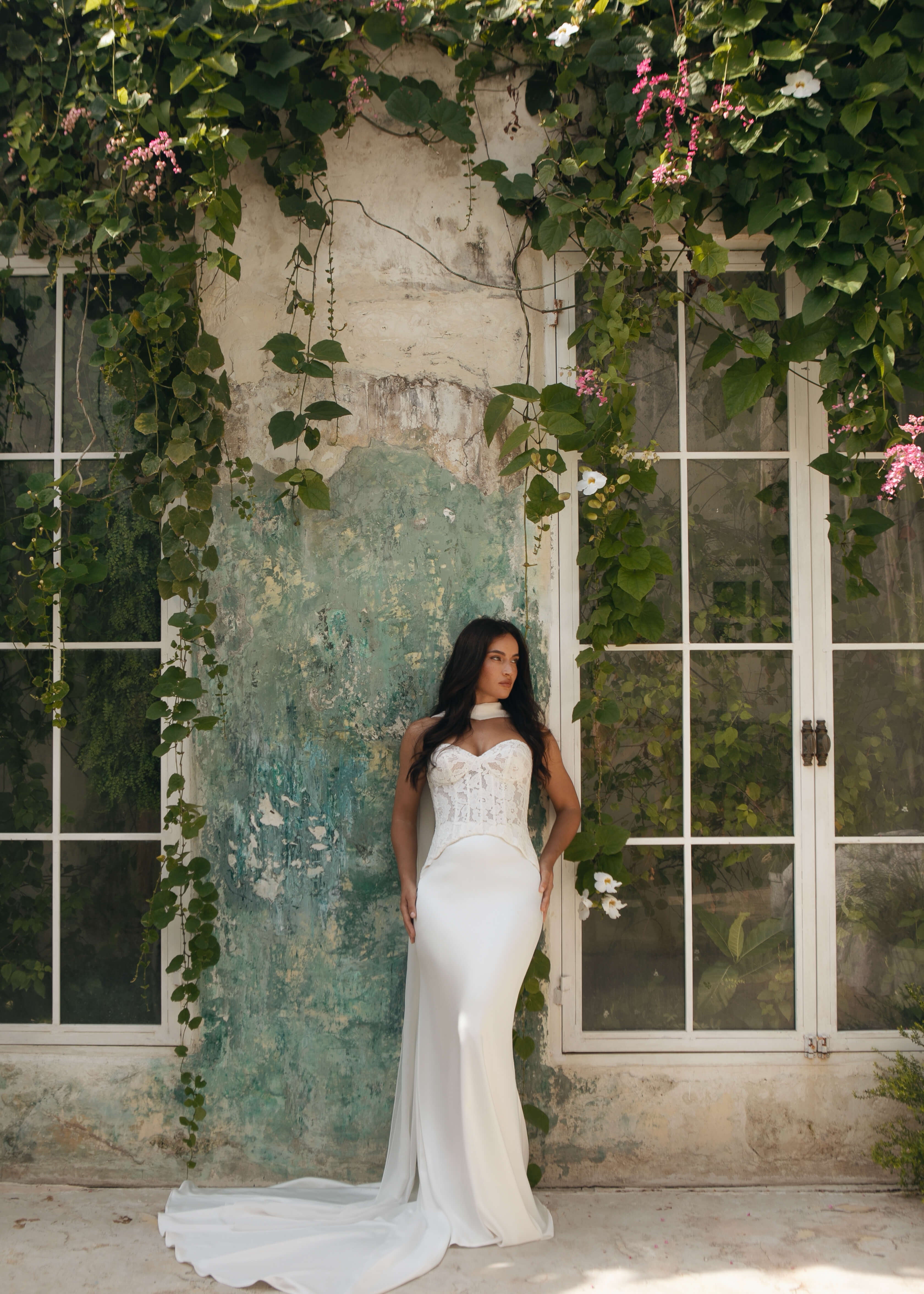 Woman in a Lace Mermaid Wedding Dress standing in a decorative indoor setting with greenery and flowers.