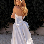 Woman in a white strapless gown standing against a dark green bush.