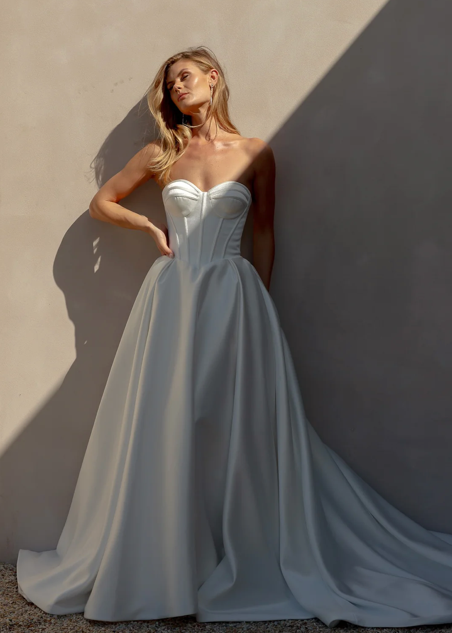 Woman in an after five textured satin A-line wedding dress standing against a textured wall.