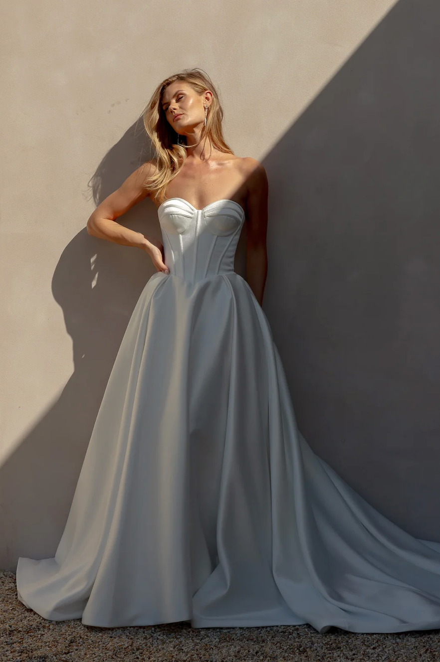 Woman in an after five textured satin A-line wedding dress standing against a textured wall.