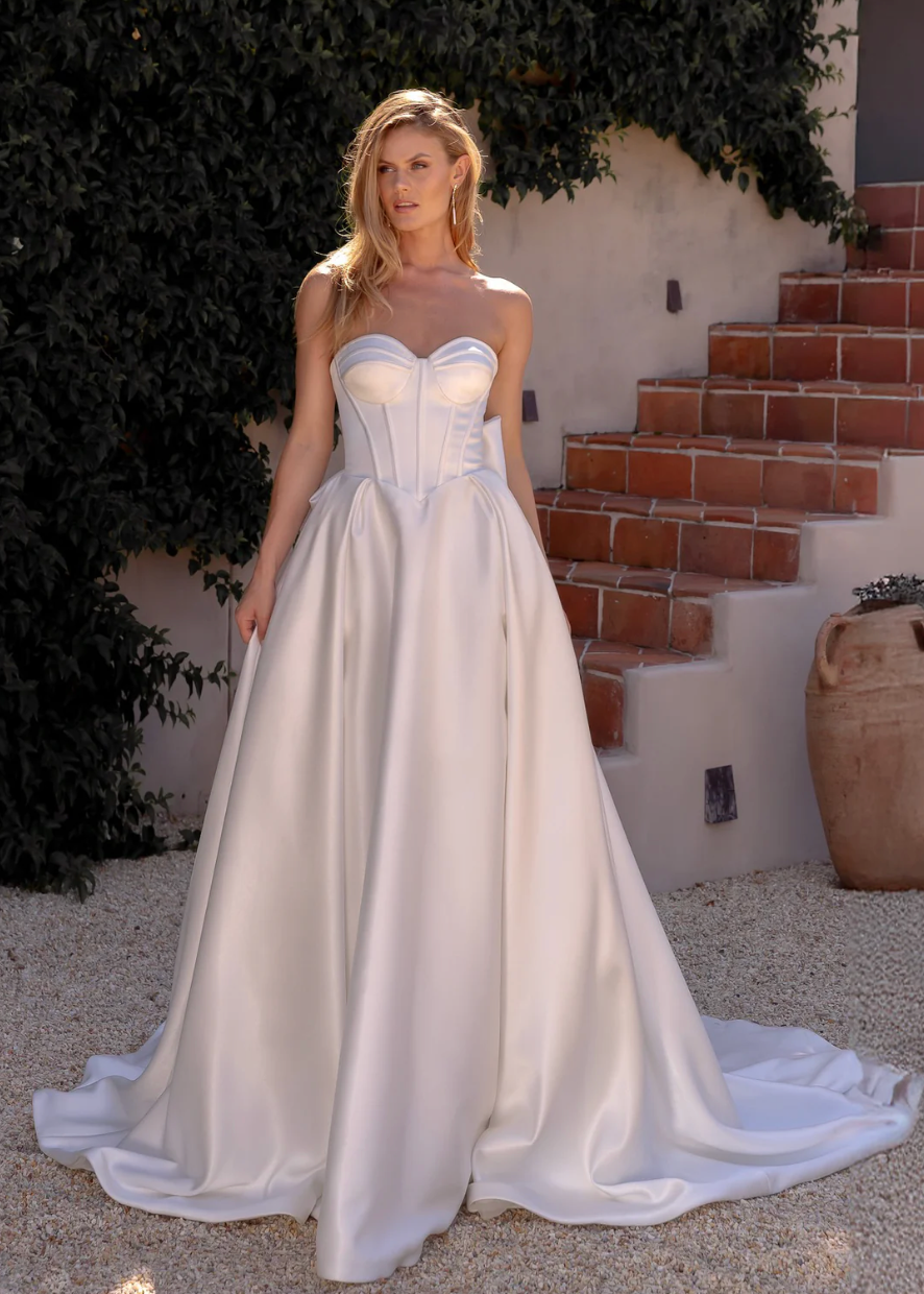 Woman in an after five textured satin A-line wedding dress standing outdoors with greenery and steps in the background