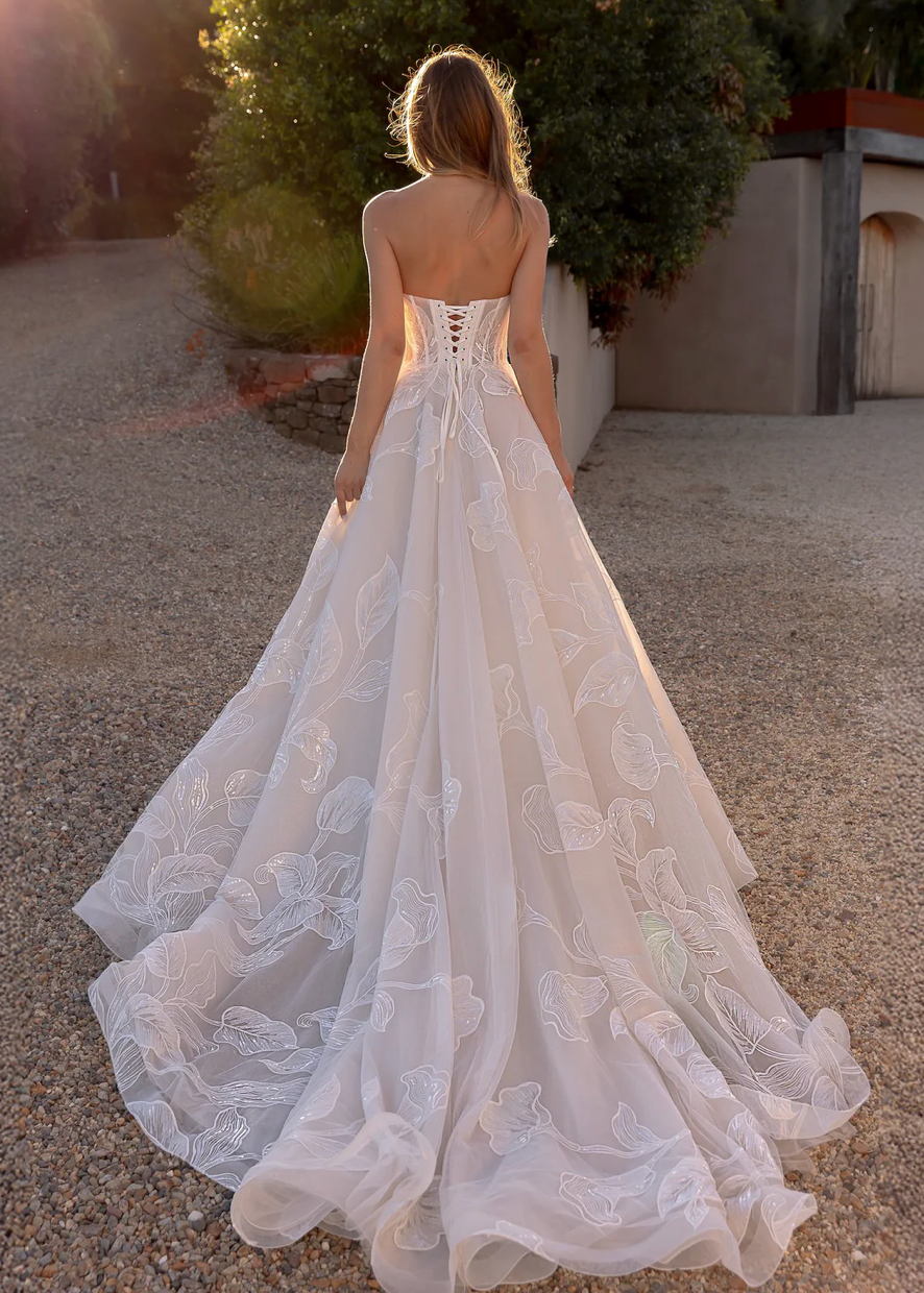 Woman in an after five lace appliqué A-line wedding dress standing outdoors with trees in the background