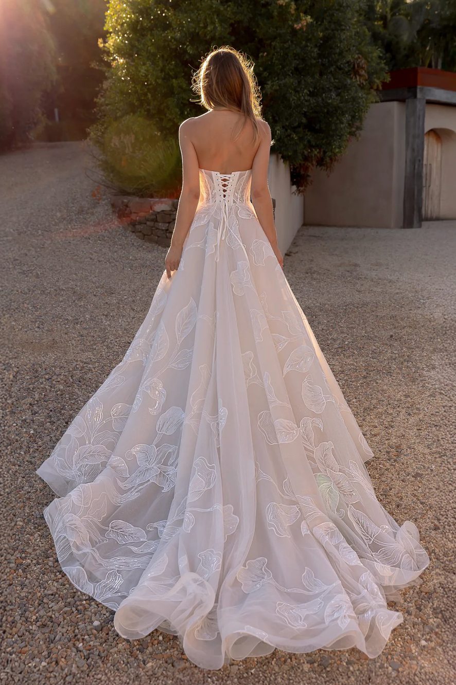 Woman in an after five lace appliqué A-line wedding dress standing outdoors with trees in the background