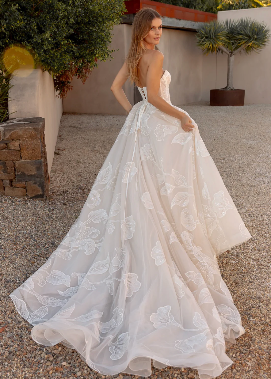 Woman in an after five lace appliqué A-line wedding dress standing outdoors with plants and stone wall in the background