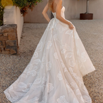 Woman in an after five lace appliqué A-line wedding dress standing outdoors with plants and stone wall in the background