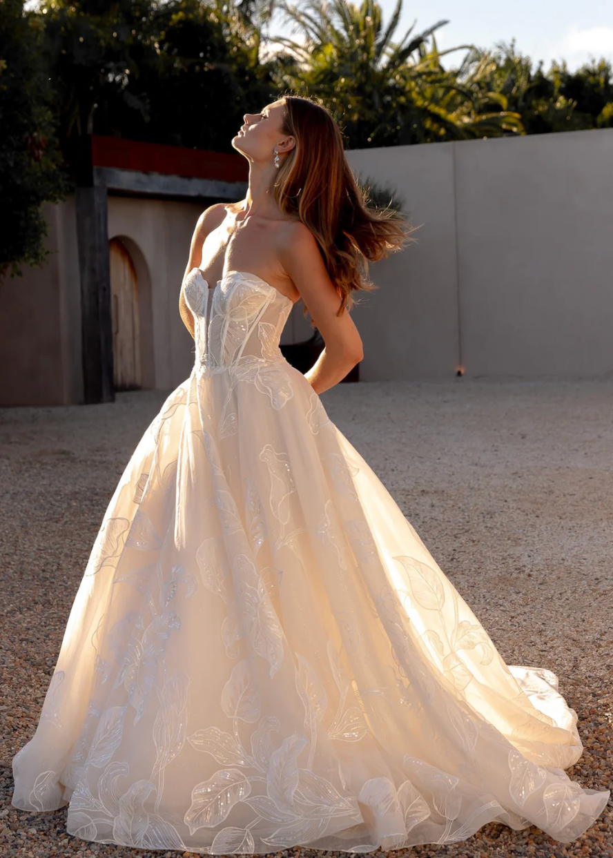 Woman in an after five lace appliqué A-line wedding dress standing outdoors with trees in the background