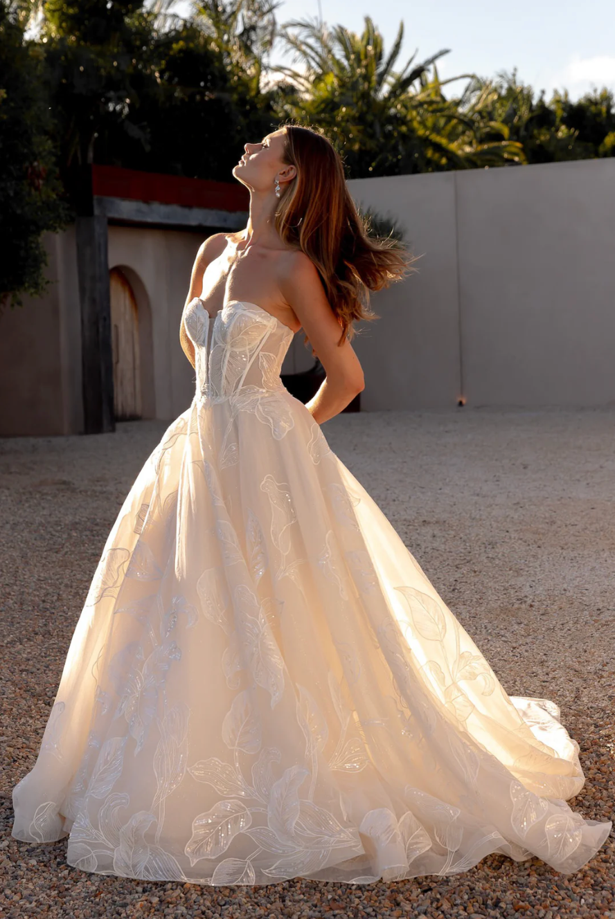 Woman in an after five lace appliqué A-line wedding dress standing outdoors with trees in the background