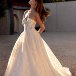 Woman in an after five lace appliqué A-line wedding dress standing outdoors with trees in the background