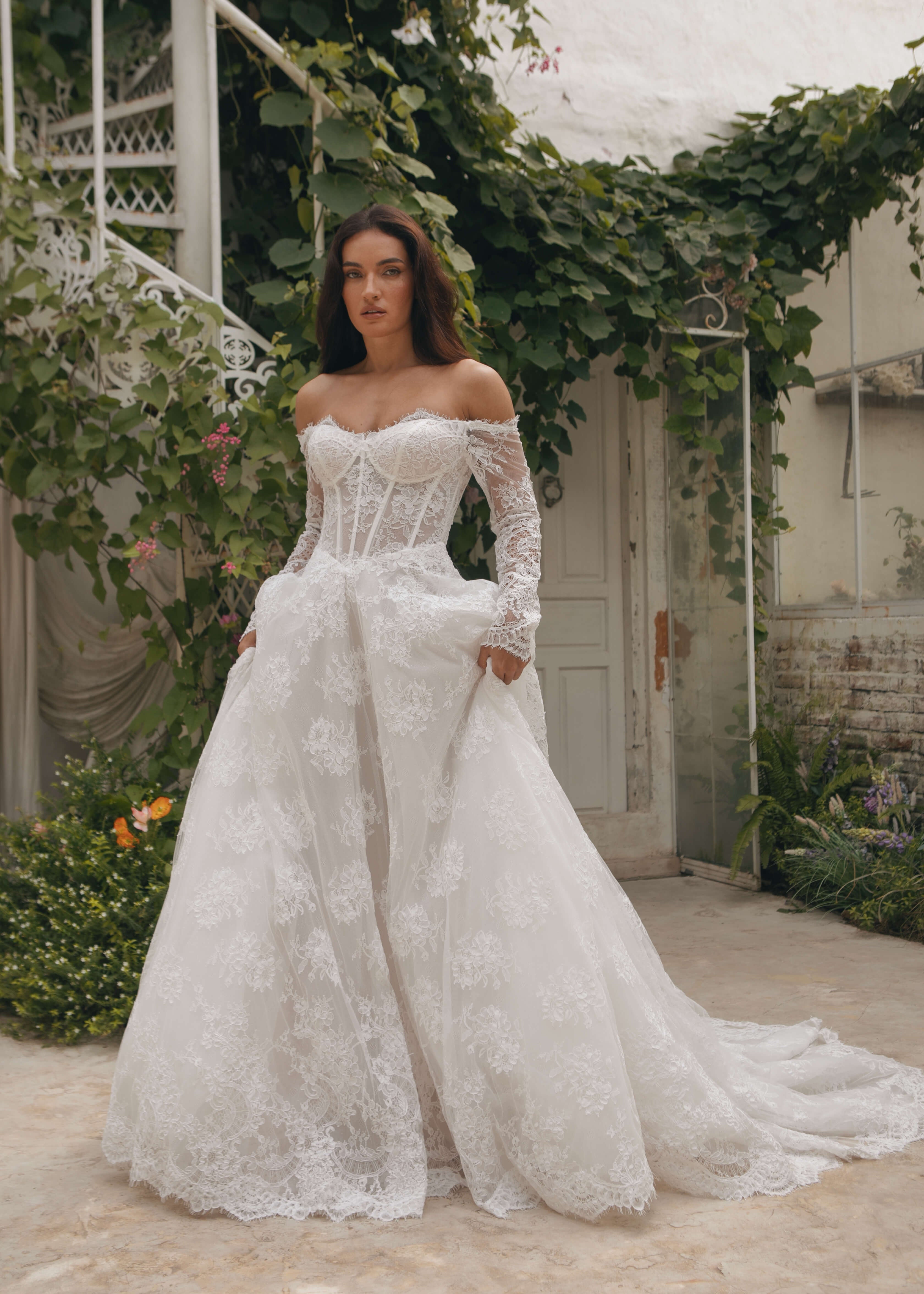 Woman in a white Lace A-Line Wedding Dress standing outdoors with greenery and a building in the background.