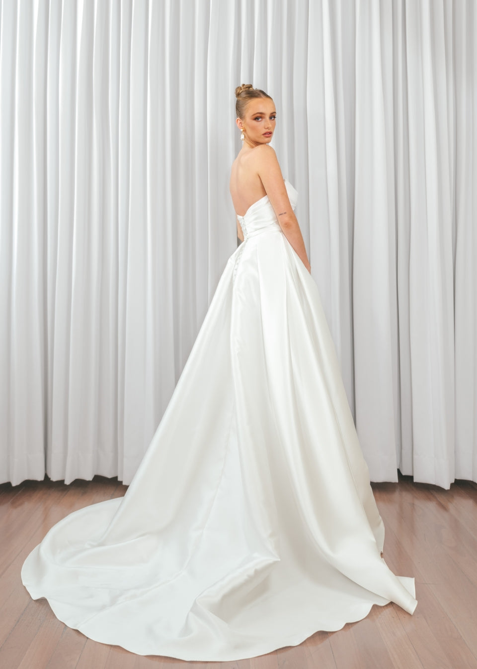 Back view of bride wearing Marigold Mikado A-line wedding dress with strapless bodice and flowing satin train.