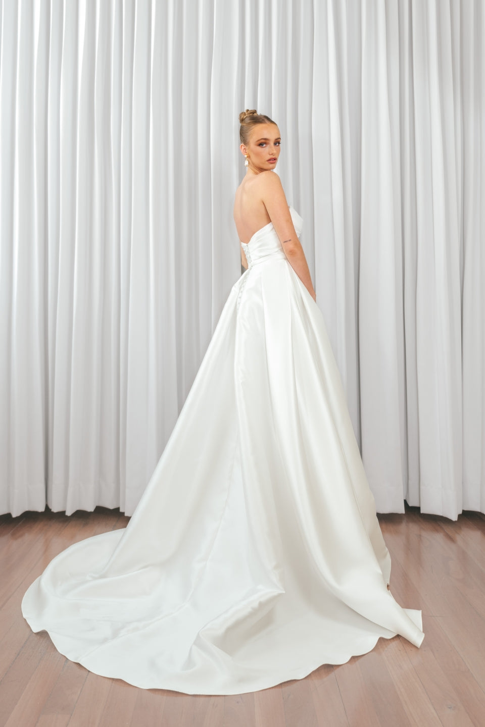 Back view of bride wearing Marigold Mikado A-line wedding dress with strapless bodice and flowing satin train.
