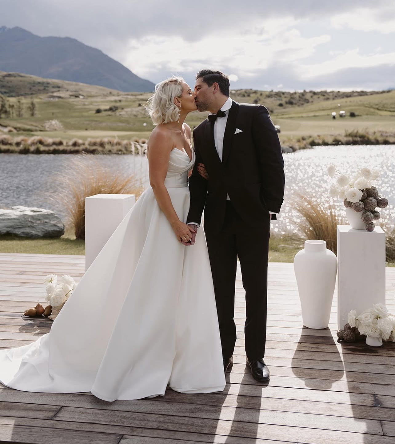 Bride wearing Marigold Mikado A-line wedding dress with strapless sweetheart bodice kissing groom at lakeside wedding ceremony.