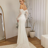 Woman in a Off Shoulder Fitted Wedding Dress standing in a room with a mirror and plants.