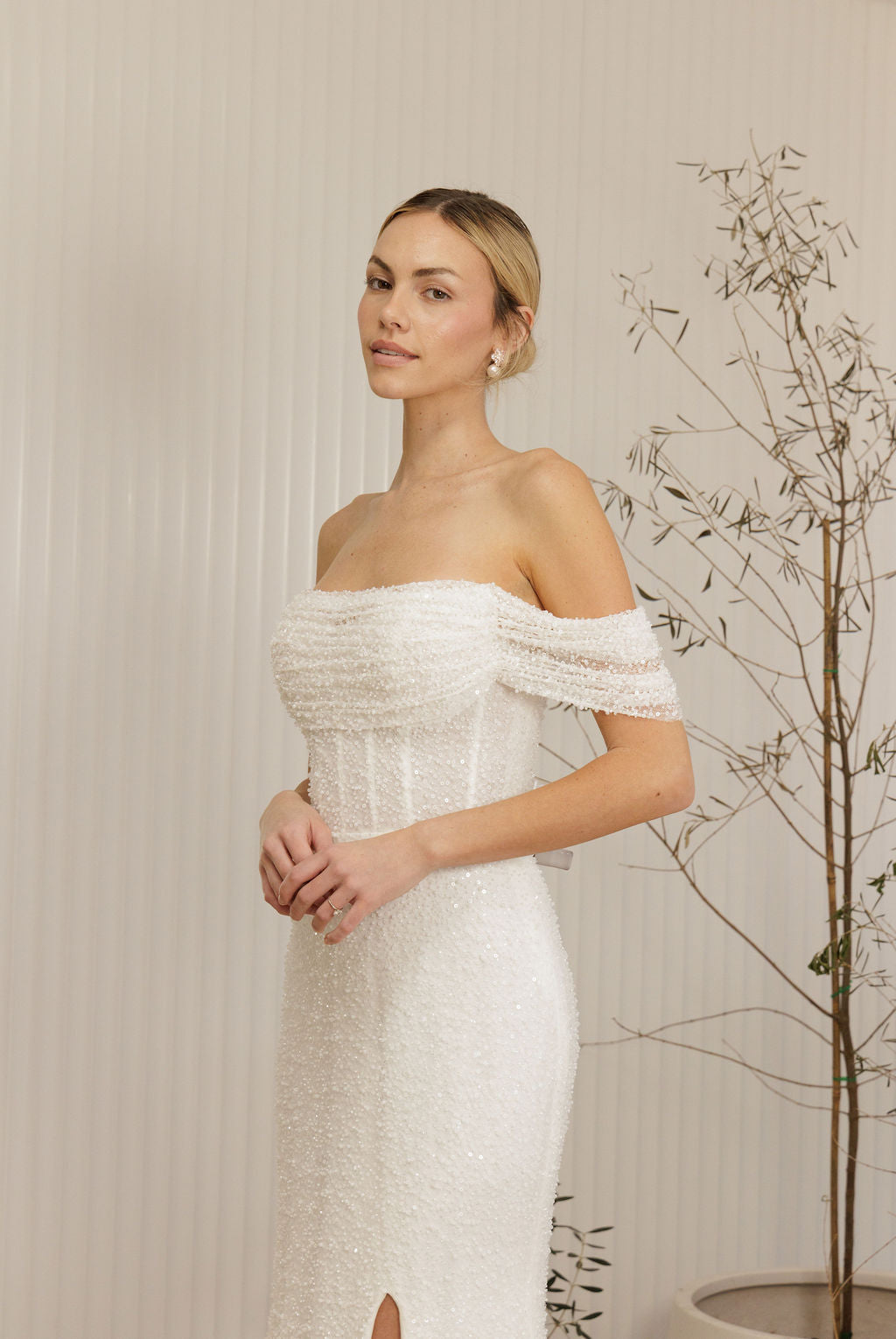 Woman wearing a Off Shoulder Fitted Wedding Dress standing against a neutral background