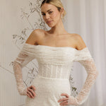 Woman wearing a Off Shoulder Fitted Wedding Dress with long sleeves in a neutral setting