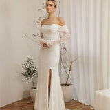 Woman wearing a Off Shoulder Fitted Wedding Dress with a high slit in a room with white curtains and plants.