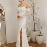 Woman in a Off Shoulder Fitted Wedding Dress standing in a room with a mirror and plants.
