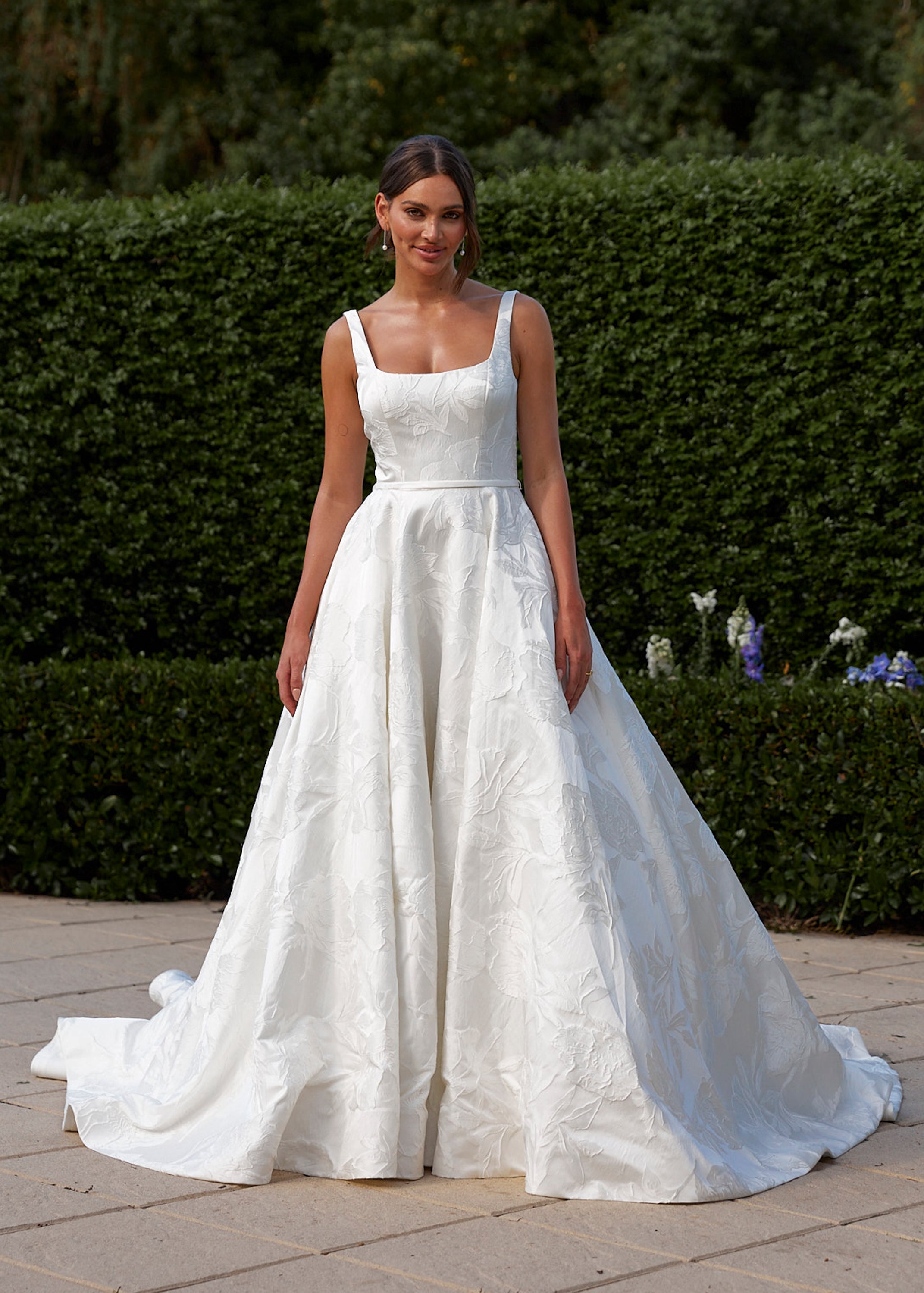 Woman in a Jacquard Satin A-Line Wedding Dress standing outdoors with greenery in the background