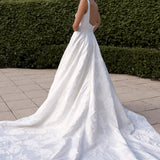 Woman in a Jacquard Satin A-Line Wedding Dress standing outdoors with greenery in the background