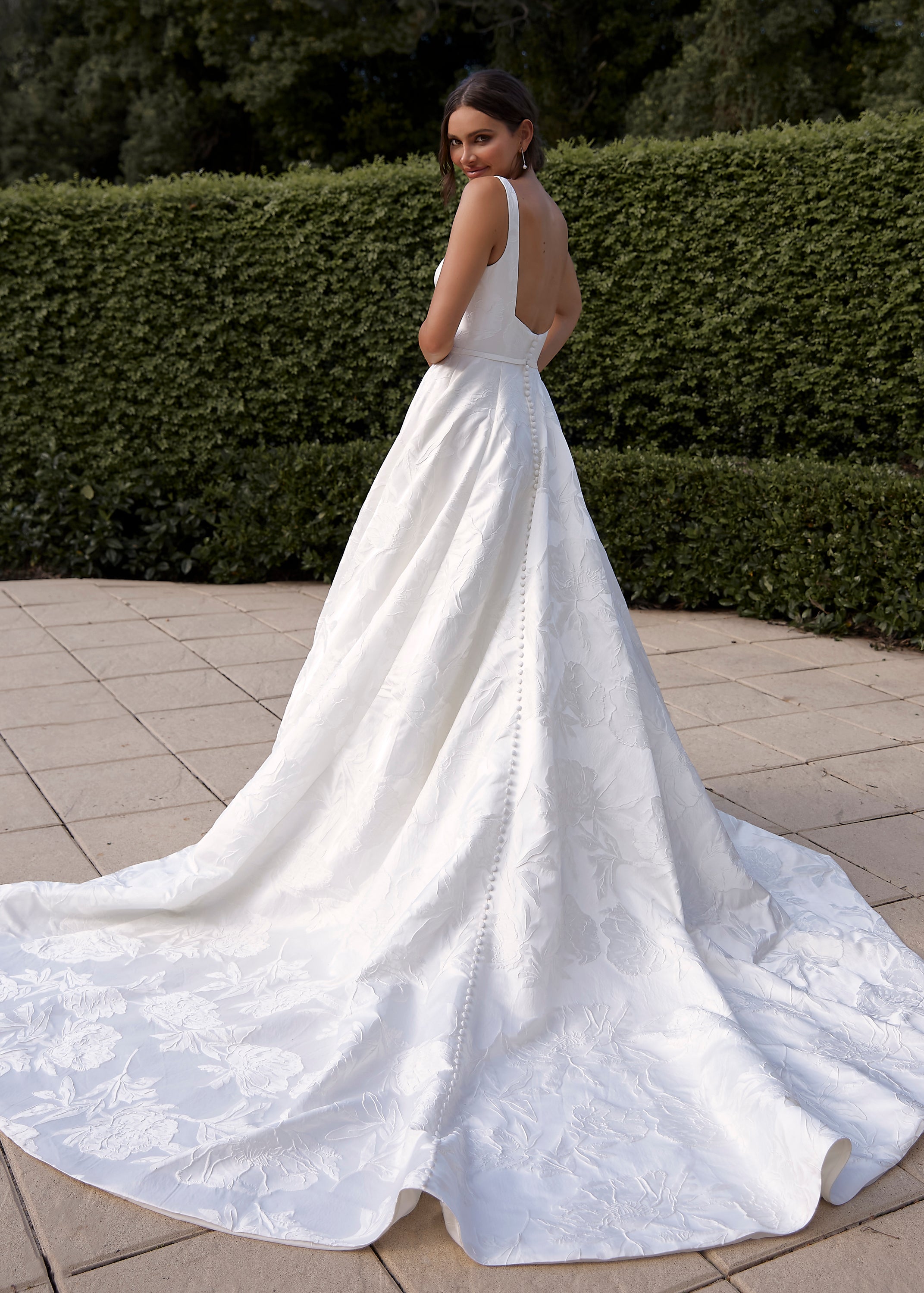 Woman in a Jacquard Satin A-Line Wedding Dress standing outdoors with greenery in the background