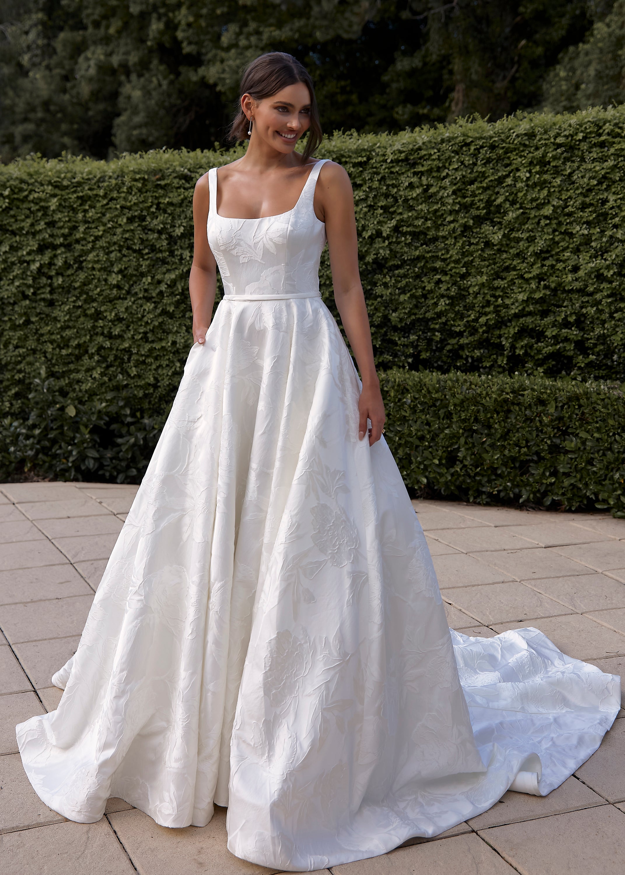 Woman in a Jacquard Satin A-Line Wedding Dress standing outdoors with greenery in the background
