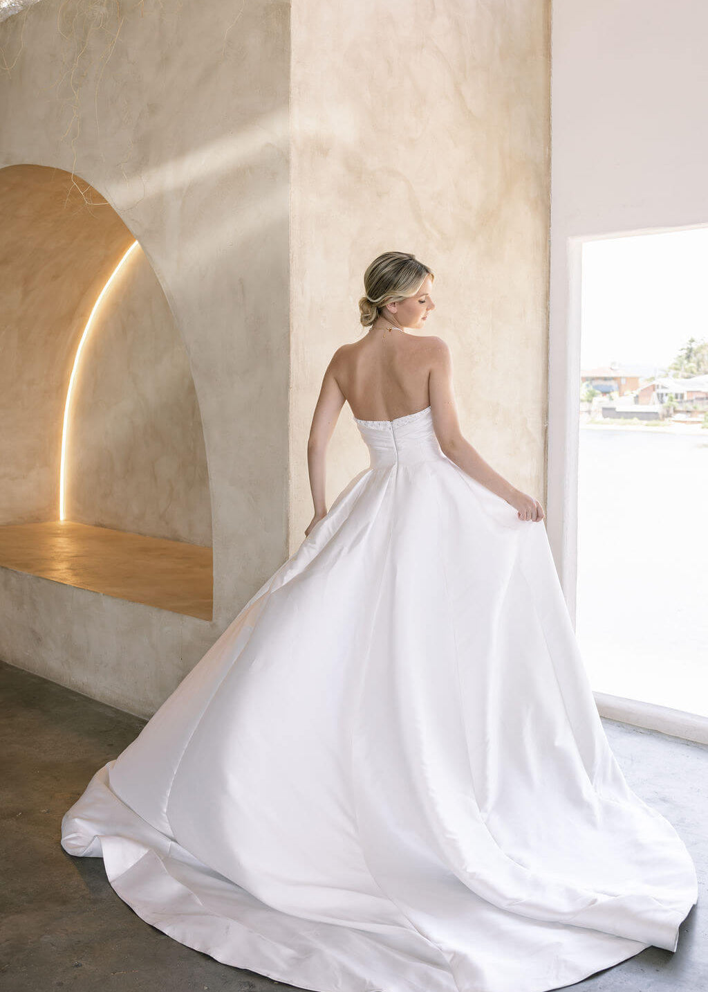 Woman in a Strapless Ball Gown Wedding Dress standing in a modern indoor setting with large windows.
