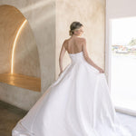 Woman in a Strapless Ball Gown Wedding Dress standing in a modern indoor setting with large windows.