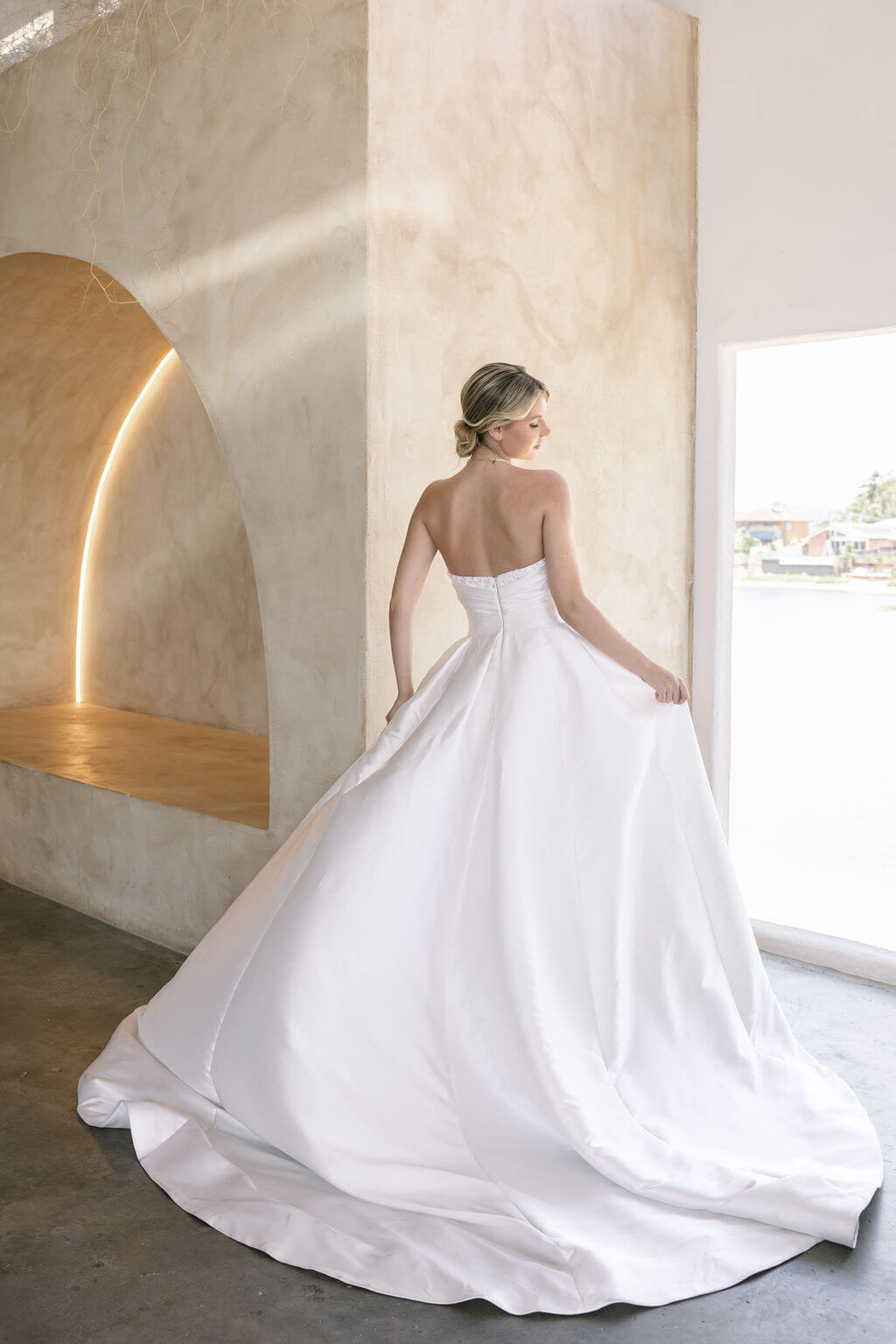 Woman in a Strapless Ball Gown Wedding Dress standing in a modern indoor setting with large windows.