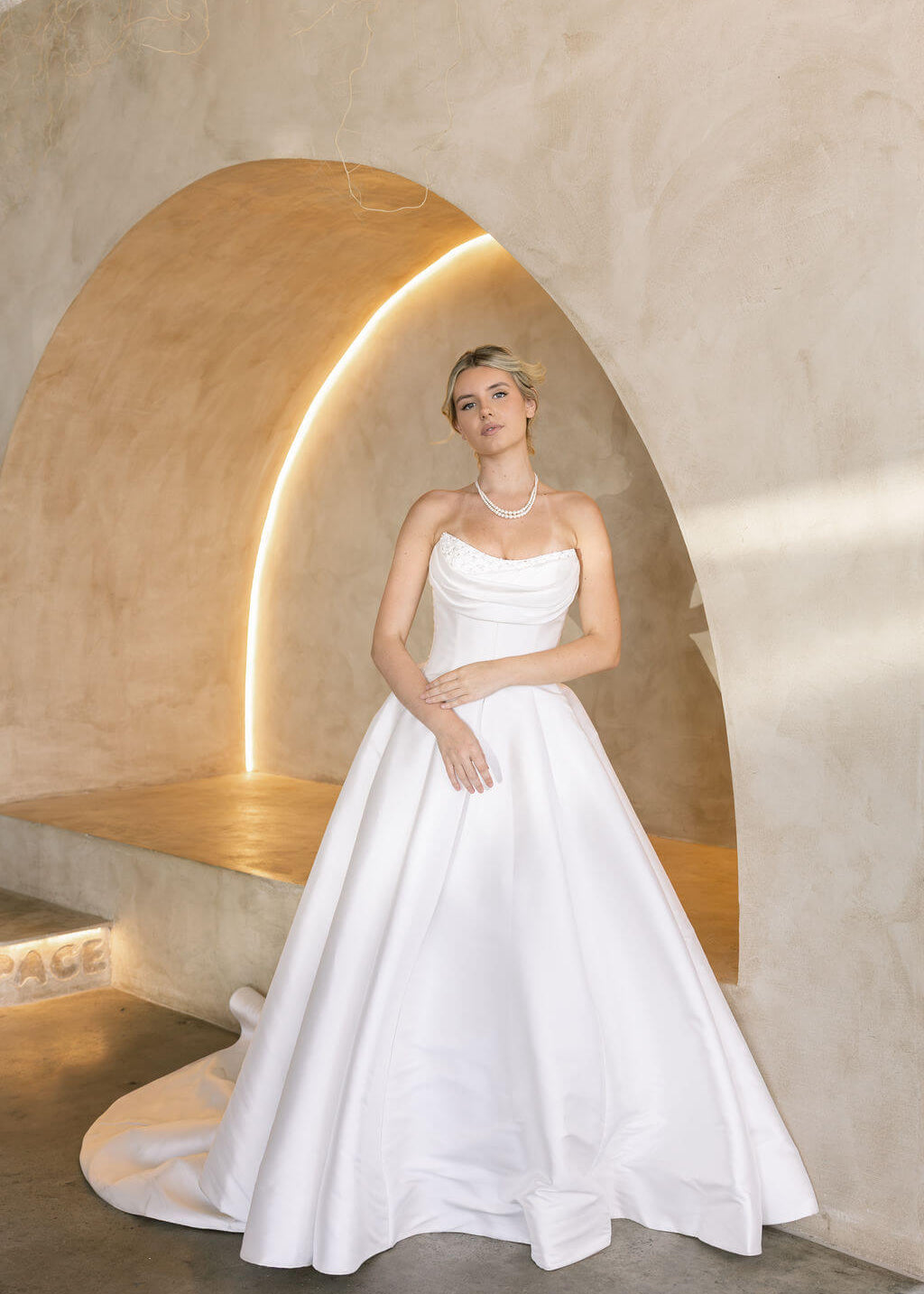 Woman in a Strapless Ball Gown Wedding Dress standing in a modern, softly lit room with a neutral color palette.