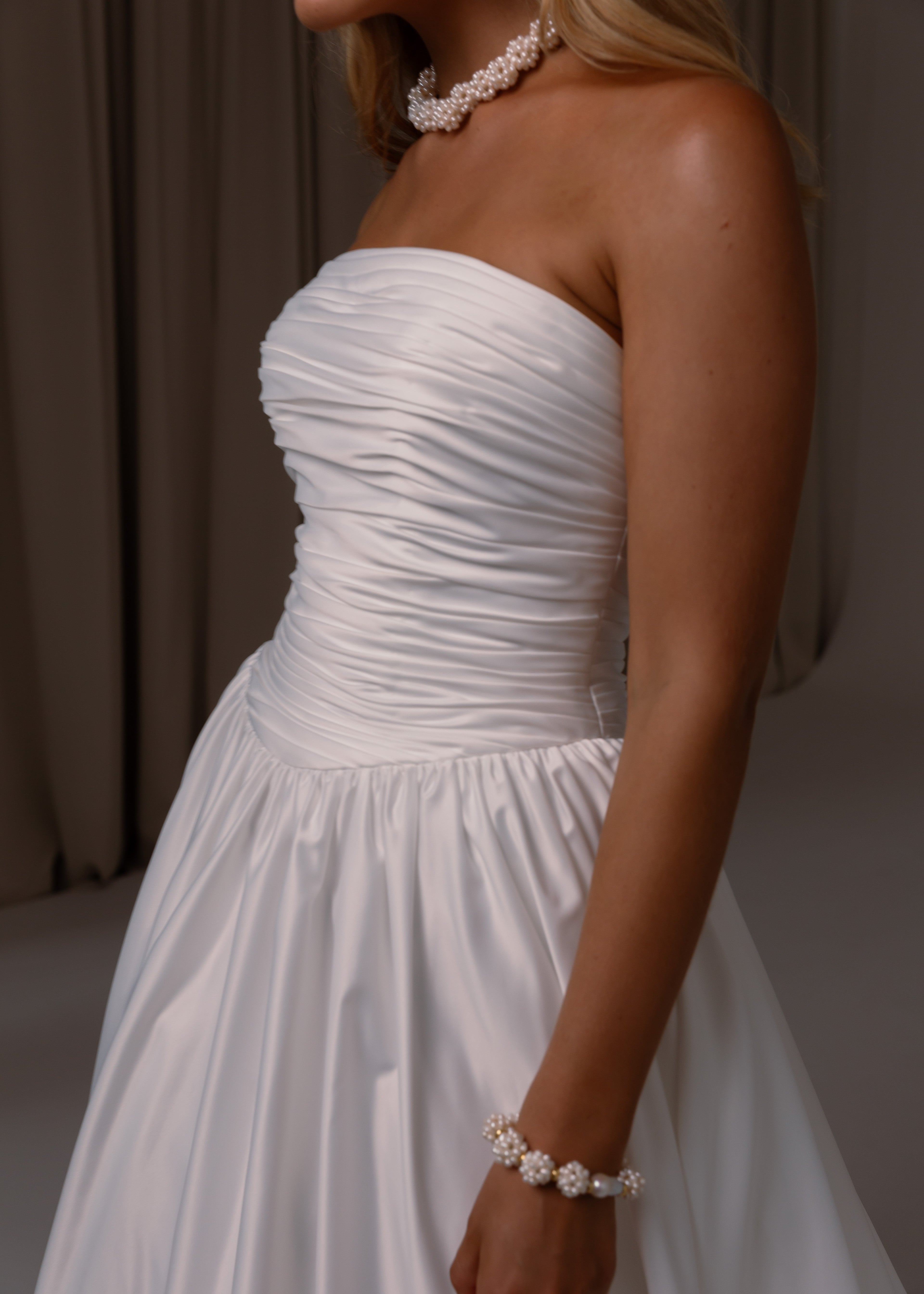 Woman wearing a Satin A-Line Wedding Dress with jewelry against a neutral background