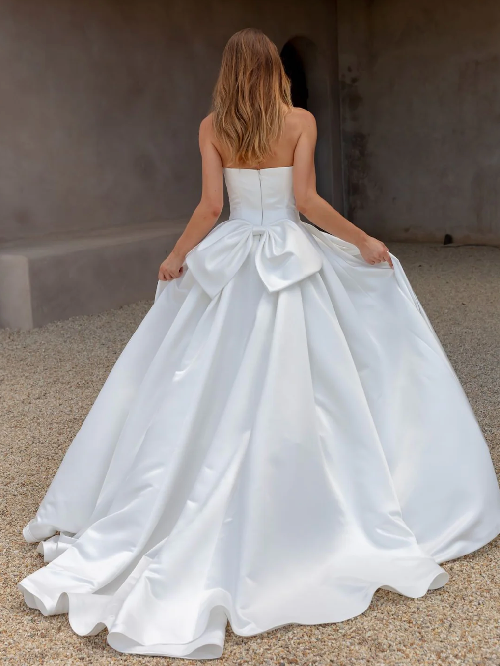 Woman wearing an AFTER FIVE heavy satin A-line wedding dress with a large bow at the back in an indoor setting.