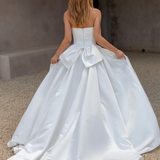 Woman wearing an AFTER FIVE heavy satin A-line wedding dress with a large bow at the back in an indoor setting.