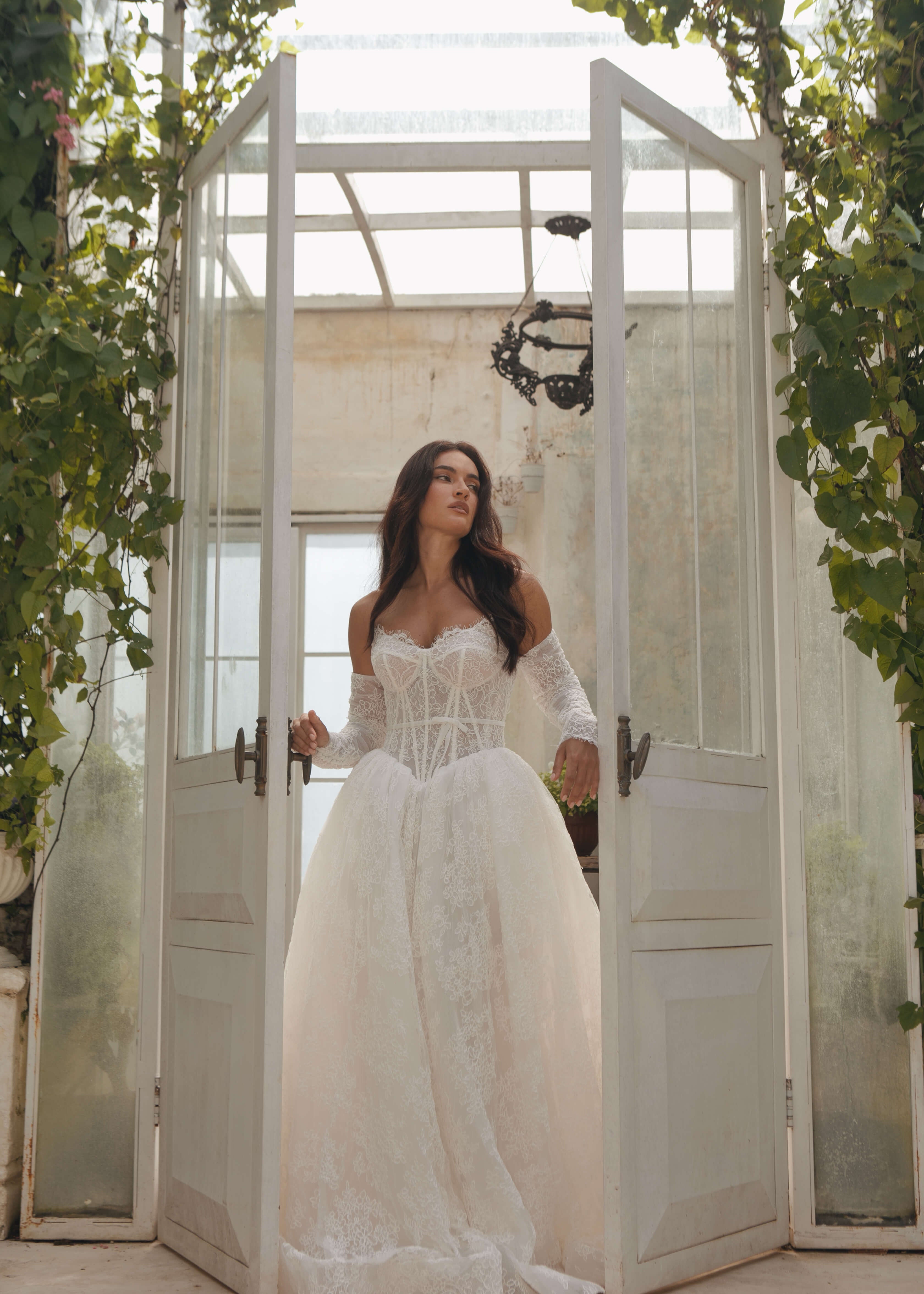 Woman in a Lace A-Line Wedding Dress standing in a greenhouse with large glass doors.