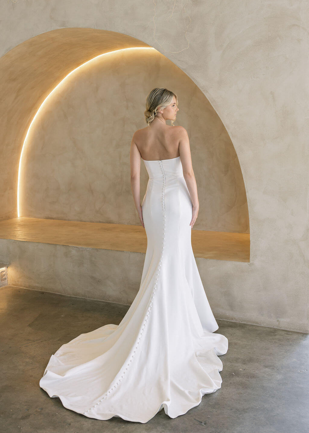 Woman in a white strapless wedding dress standing in front of a modern architectural arch.
