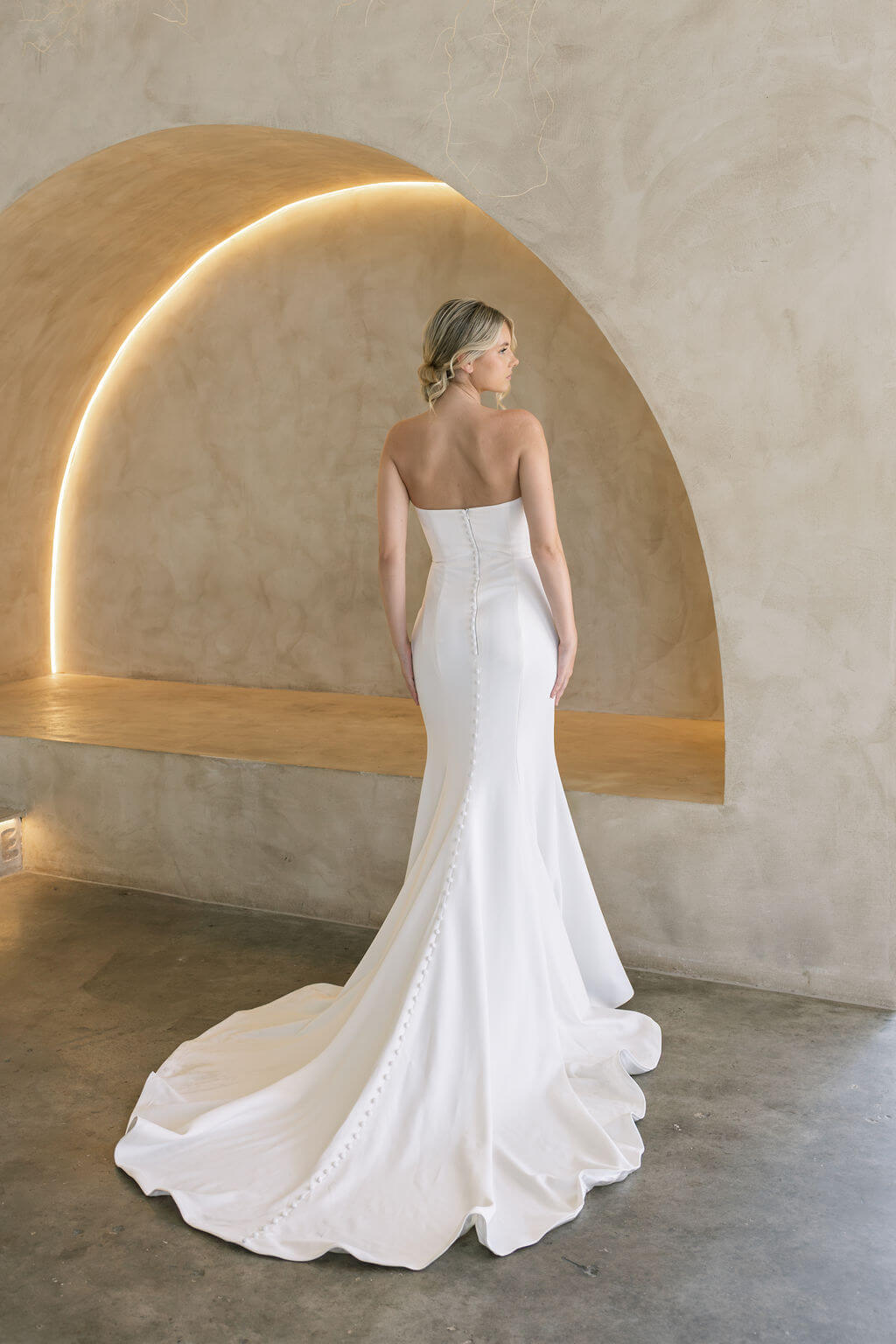 Woman in a white strapless wedding dress standing in front of a modern architectural arch.