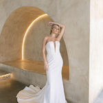 Woman in a modern crepe fit-and-flare wedding dress standing against a modern architectural background