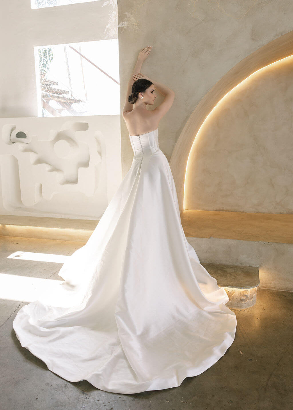 Woman in a white Vermont Mikado wedding dress standing in a modern indoor setting with light-colored walls.