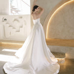 Woman in a white Vermont Mikado wedding dress standing in a modern indoor setting with light-colored walls.