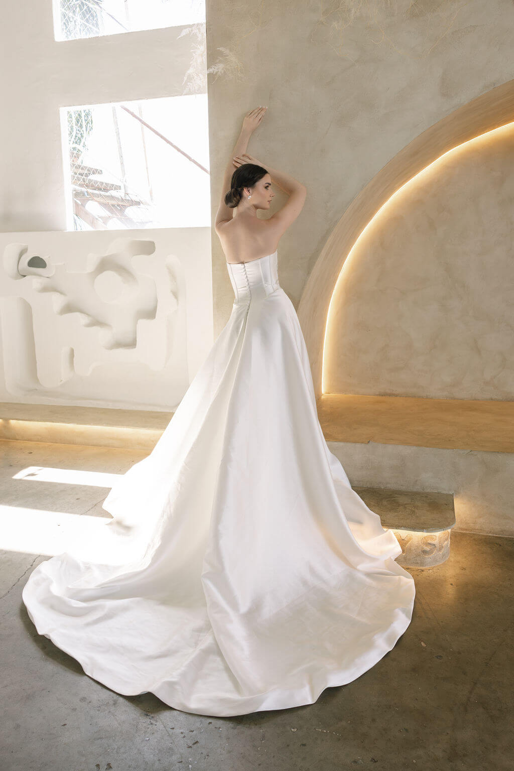 Woman in a white Vermont Mikado wedding dress standing in a modern indoor setting with light-colored walls.