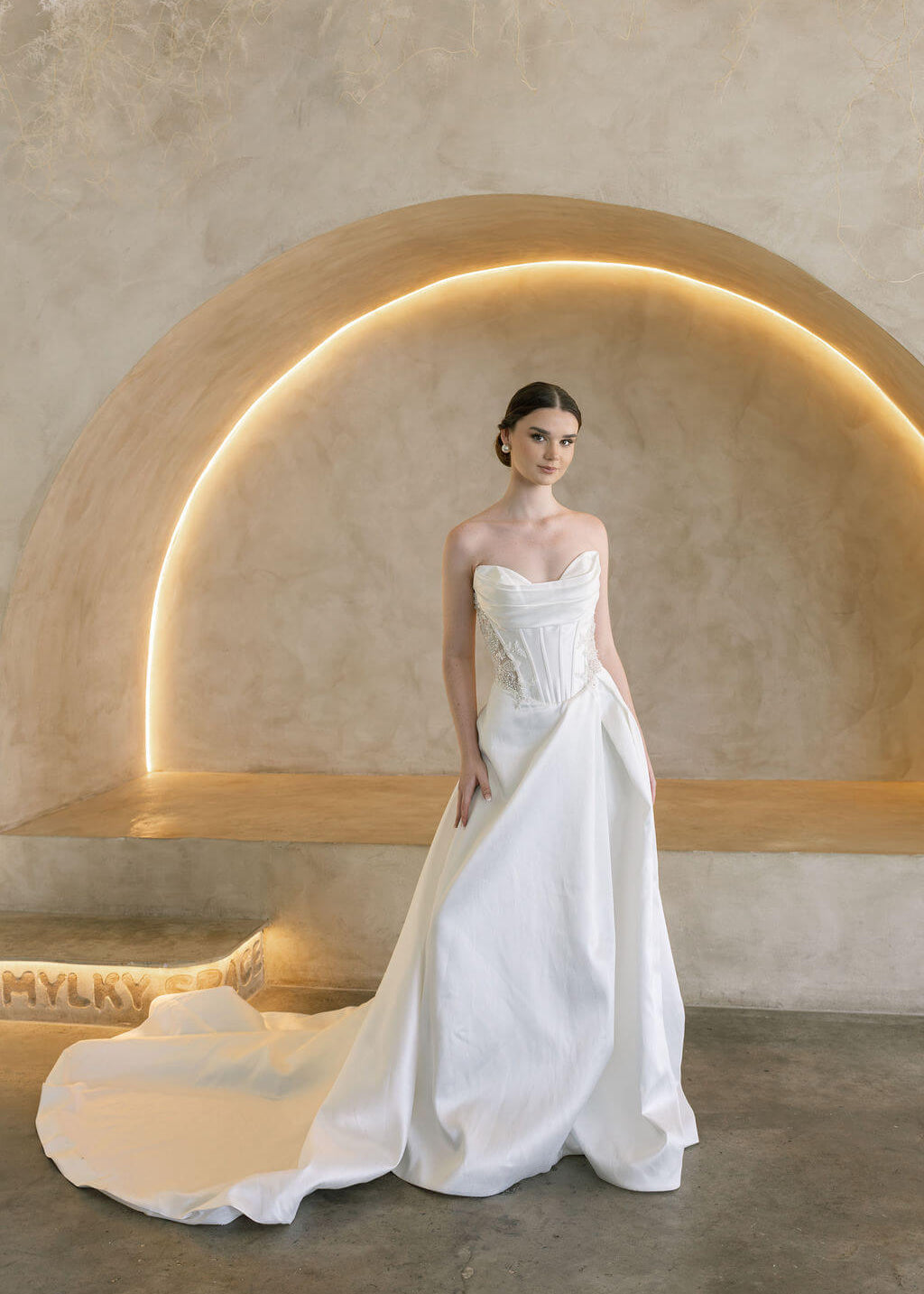 Woman in a white Vermont Mikado wedding dress standing in a modern, softly lit room.