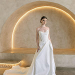 Woman in a white Vermont Mikado wedding dress standing in a modern, softly lit room.