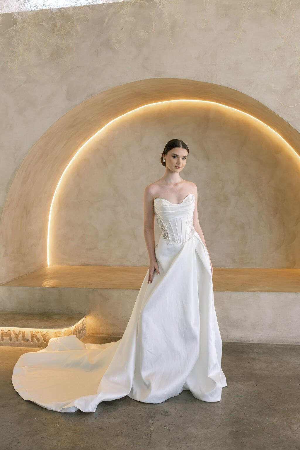 Woman in a white Vermont Mikado wedding dress standing in a modern, softly lit room.