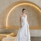 Woman in a white Vermont Mikado wedding dress standing in a modern, softly lit room.