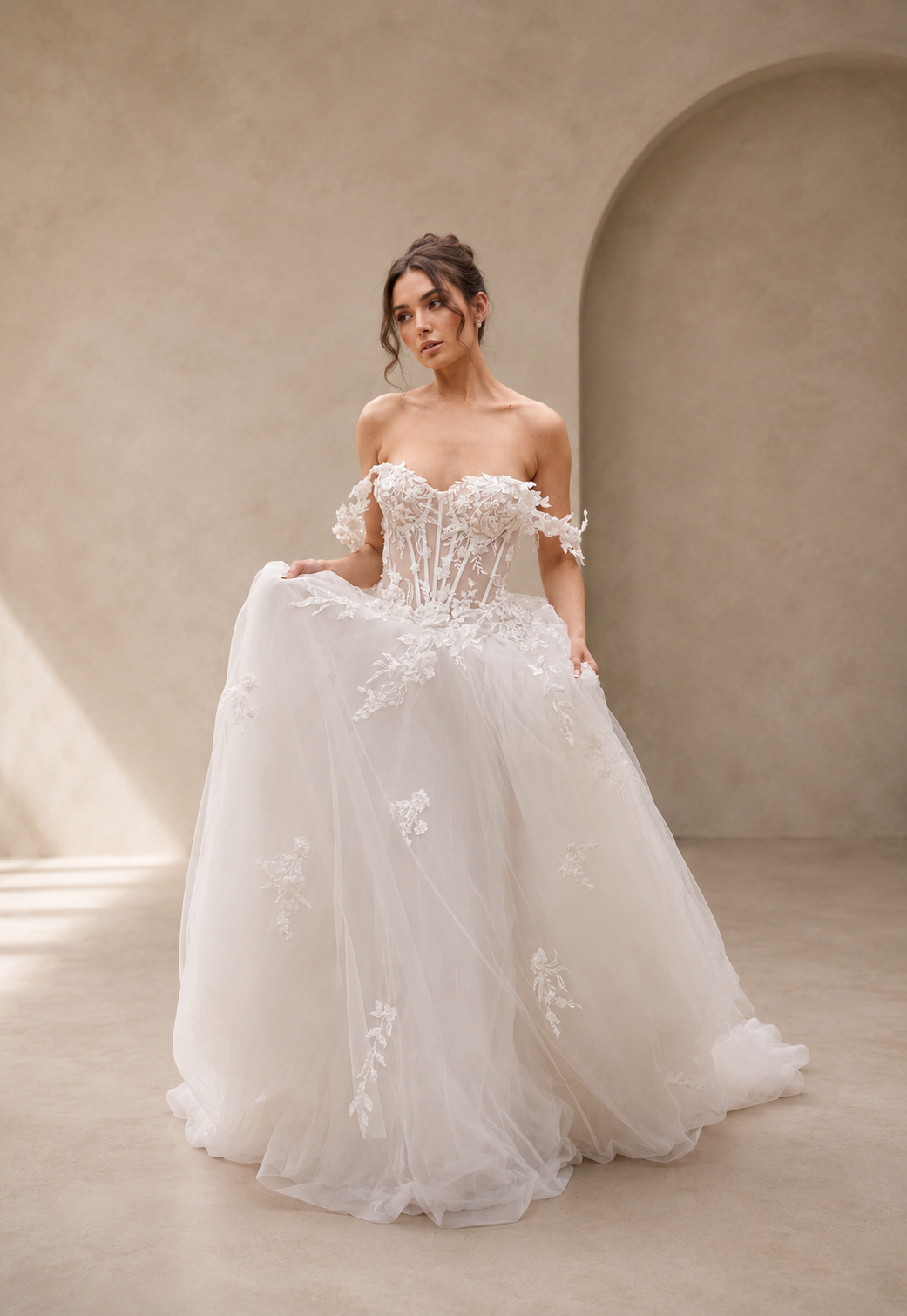 Woman wearing a white wedding dress with floral details in a softly lit room.