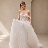 Woman wearing a white wedding dress with floral details in a softly lit room.